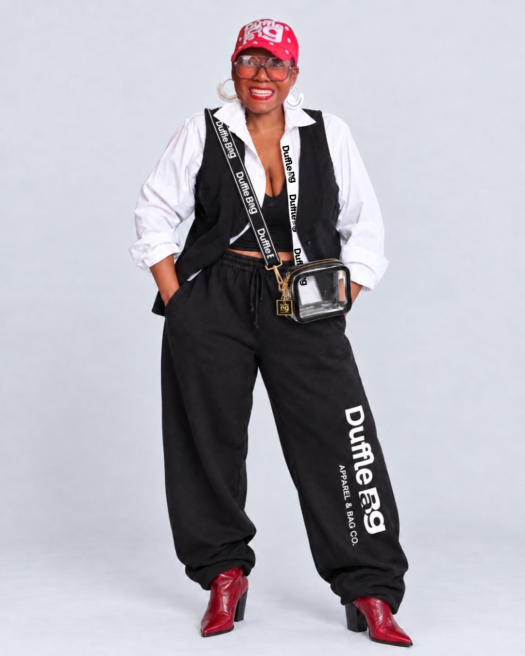 Woman modeling Duffle Bag wide-leg joggers, a clear crossbody bag by Duffle Bag Apparel, and red cowboy boots.