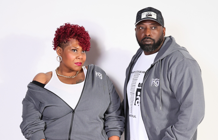 Two people wearing matching gray tracksuits with a red handbag on a white background