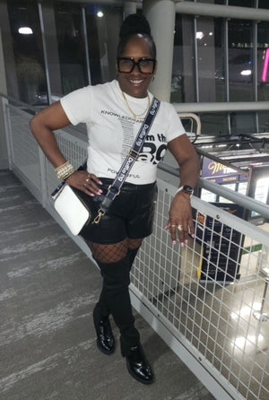 Person standing on a balcony at night with city lights in the background wear Duffle Bag Apparel Affirmation tee and Journey camara bag