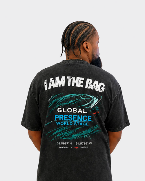 Person wearing a Duffle Bag black t-shirt with I AM THE BAG and graphics on the back, standing against a gray background