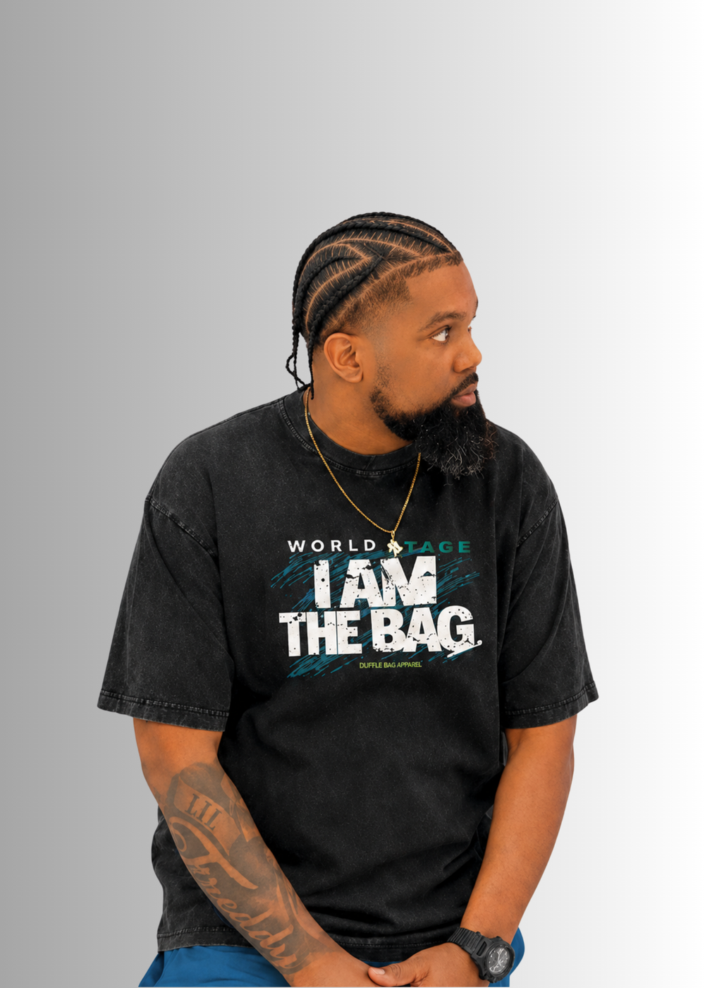 Man wearing a Duffle Bag black t-shirt with I AM THE BAG, sitting against a gray background
