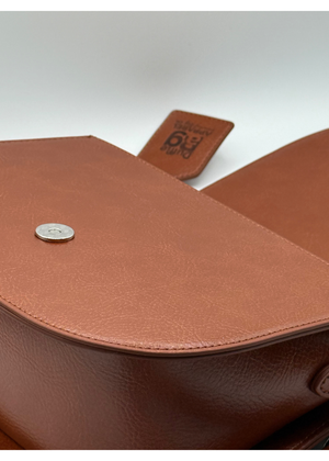 Close-up of  #camel brown leather bag with a visible Duffle Bag tag on a light gray background