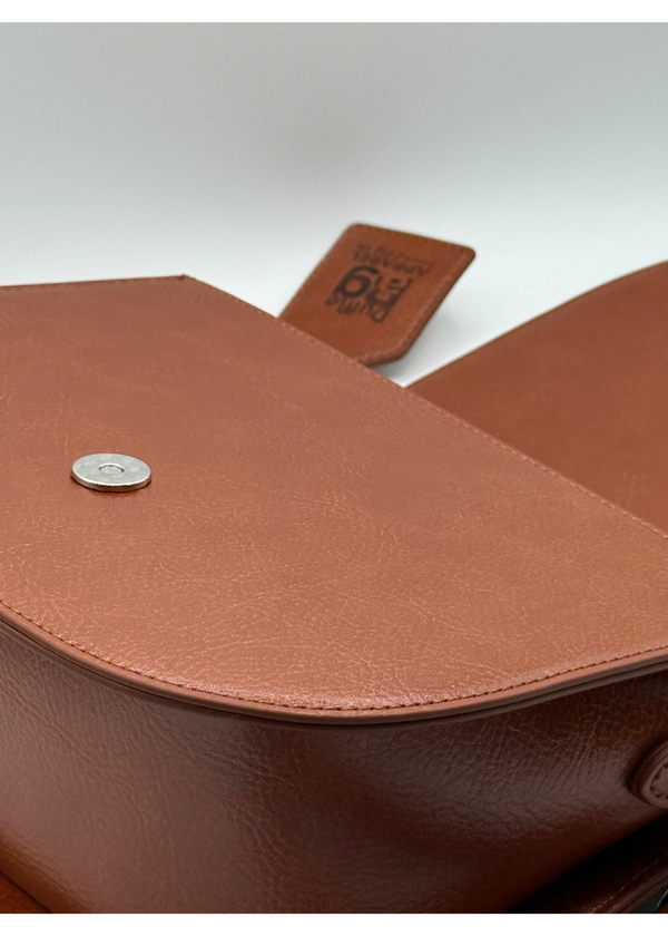 Close-up of  #camel brown leather bag with a visible Duffle Bag tag on a light gray background