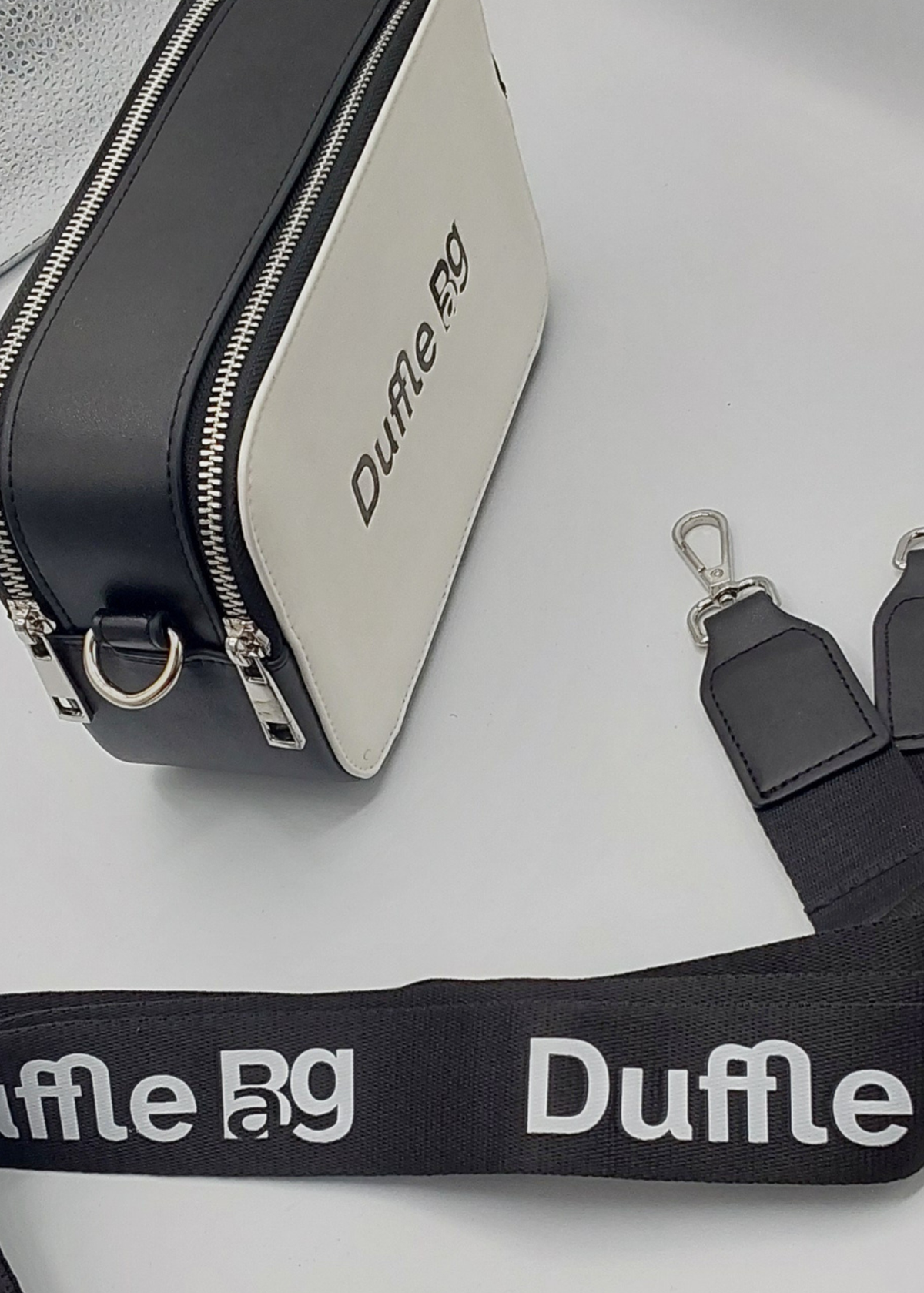 Black and silver duffle bag with visible 'Duffle Bg' branding on a light gray background