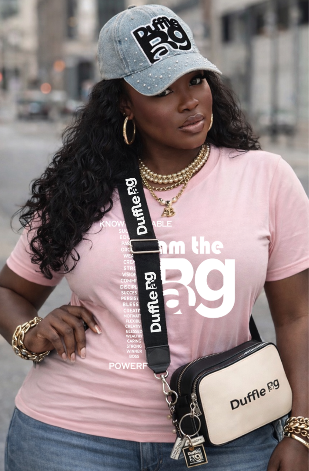 Woman wearing a pink t-shirt with 'I Am the BAG T-shirt, holding a Duffle Bag branded bag.